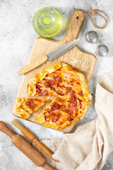 Galette or pie with turkey meat and parmesan and mozzarella cheeses on a serving board on a gray wooden culinary background closeup. Delicious homemade hearty pastries	
