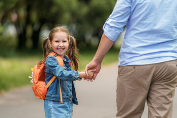 loving family. a caring dad accompanies a little girl with backpacks to school. The child smiles...