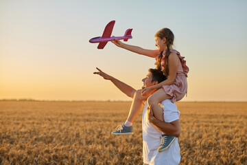 girl riding on father's shoulder and playing with toy airplane