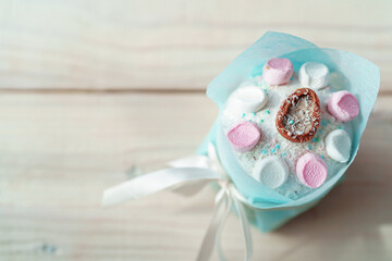 Easter composition. A glazed Easter cake decorated with sugar sprinkles, marshmallows and a chocolate egg, beautifully packaged, stands close-up on a light wood table. Free space