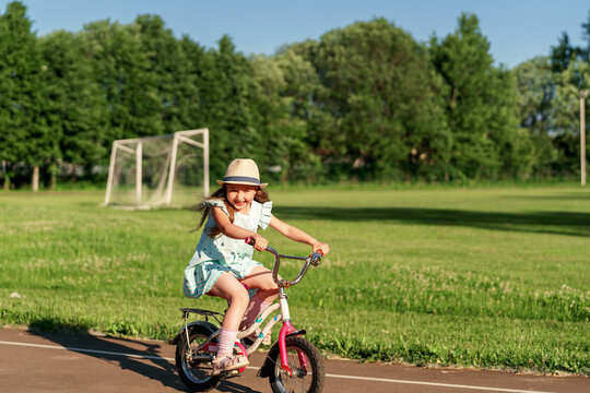 little cute girl rides and rides a bicycle at the stadium. The child enjoys riding and gets a new skill. Keeps the balance. Dynamic image