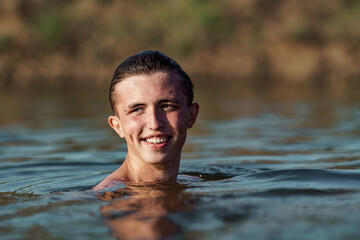 smiling young attractive man swims in a river or lake, enjoys and refreshes himself from swimming. The freshness wild nature. Relaxation and active summer vacation. Swimming skills. Dive into water