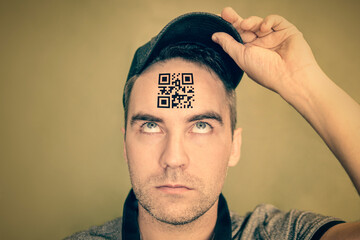 young man with a qr code on his forehead. A man with a stupid expression looks at his qr code on his head. The concept of chipping the population. global control and governance