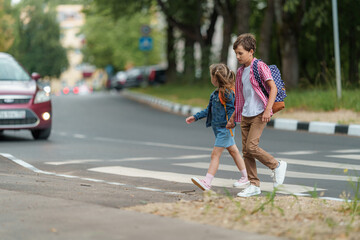 girl and boy with backpacks carefully cross road on pedestrian crossing on their way to school. Traffic rules. Walking path along zebra in city. concept of pedestrians crossing pedestrian crossing. - obrazy, fototapety, plakaty