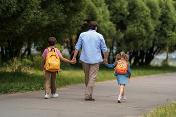 loving family. a caring dad accompanies cheerful children, a boy and a girl with backpacks, to...