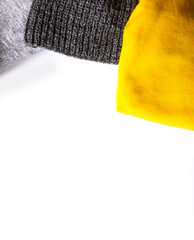 Warm winter wear on white background. Copy space. Yellow and grey trendy fashion colors. Knitted jumper and plaid