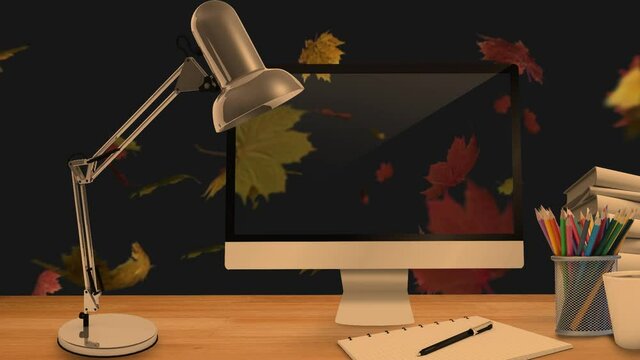 Desktop computer and office equipment on a table against autumn maples leaves floating in background