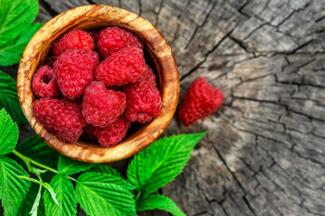 Fresh juicy raspberries in wooden bowl. Summer still life with raspberries on an old wooden table. Copy space .Jar of raspberry jam and fresh berries on wooden background