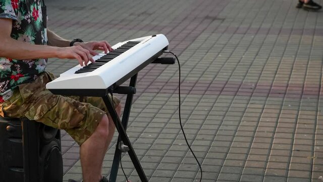 Close-up view of male street performer playing on white digital piano on city square at sunset. 4K resolution video. Music theme.
