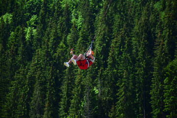 A young man jumped from bungee jumping and now hangs on a rope and films himself on a sports video camera against a blurred background of a green forest © Serhii