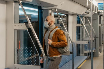 A bald man with a beard in a face mask is leaving a subway car.