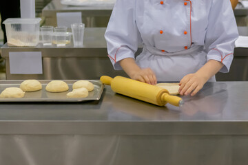 Baker, chef hands kneading fresh dough on round wooden board on kitchen table at cuisine of...