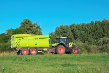 Obraz premium A rural tractor with a trailer is driving along the road.