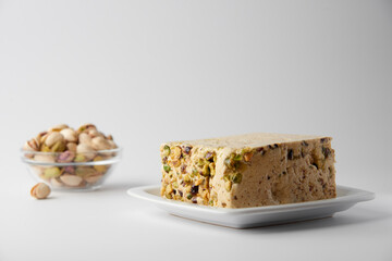 Organic halva with pistachios on a white plate isolated on white. Traditional middle eastern sweets. Jewish, turkish, arabic oriental national dessert. Turkish delight concept. Natural vegan product.