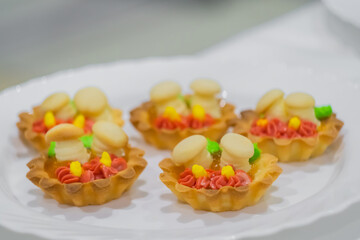 Assortment of delicious fresh shortcrust tart cakes with cream and sweet mushrooms on white plate for sale at restaurant, cafe - close up. Dessert, culinary and confectionery concept