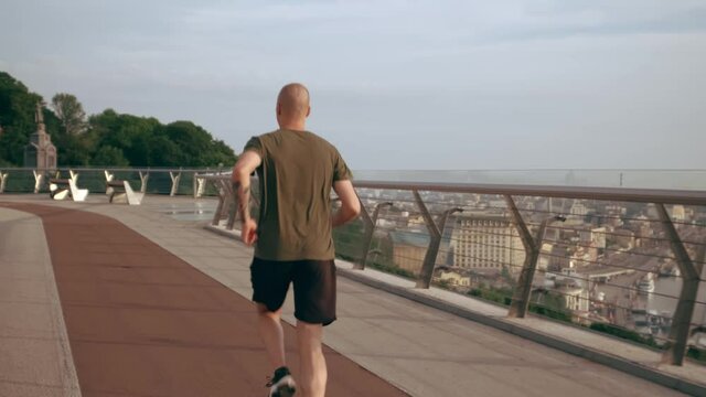 Young man in sports uniform runs on the pedestrian bridge at dawn. Slow motion. High quality 4k footage