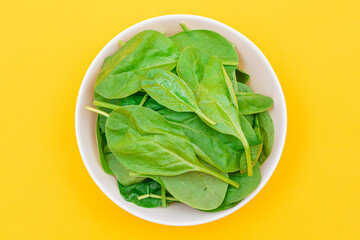 Fresh Baby Spinach Leaves in White Bowl on Yellow Background - Top View. Vegan and Vegetarian Culture. Raw Food, Green Leaves. Healthy Diet