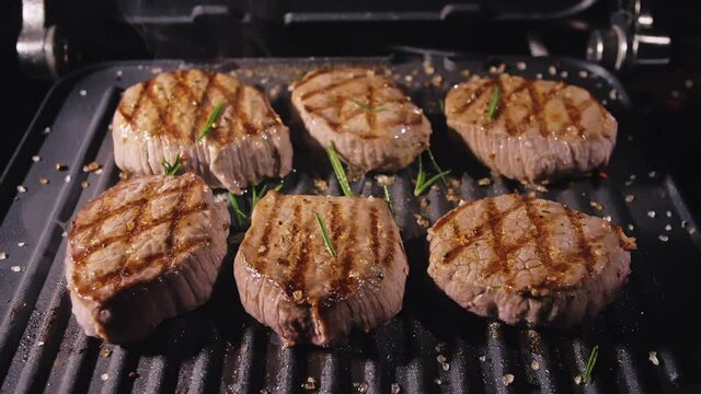 Delicious juicy meat steak cooking on grill. Aged prime rare roast grilling tenderloin fresh marble tenderness beef. Prime beef fry on electric roaster, rosemary, black pepper, salt. Slow motion.