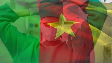 Cameroon flag waving against caucasian female surgeon wearing face mask at hospital - Powered by Adobe