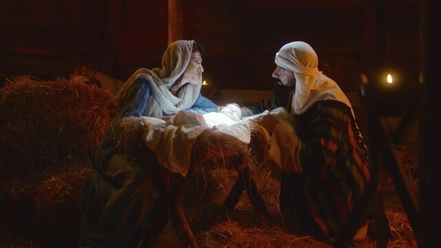 Mary and Joseph caressing baby Jesus in illuminated manger nativity scene