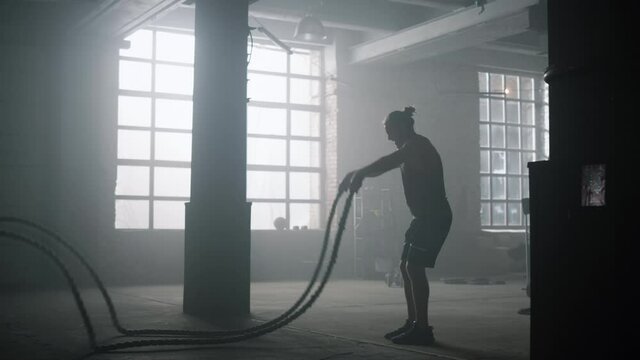 Guy battling ropes during training session. Sportsman performing intense workout