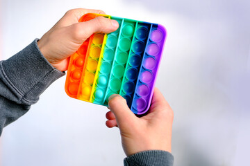 male hand holding a rainbow Toy antistress Pop it, press rubber bubbles, concept entertainment,...