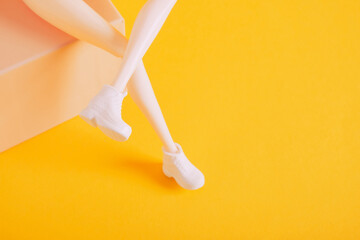 doll feet in sneakers on a gift box yellow background