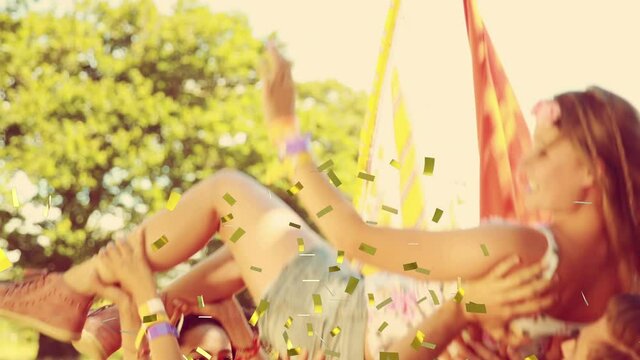 Animation of gold confetti falling over happy woman being thrown in air by friends outdoors