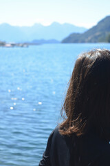 young woman with black hair from behind looking at the water of a lake and the sun