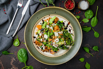 salad with pumpkin, cheese and herbs, cashews on grey plate on dark concrete table top view