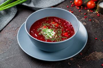 Borscht with sour cream and greens on dark concrete table