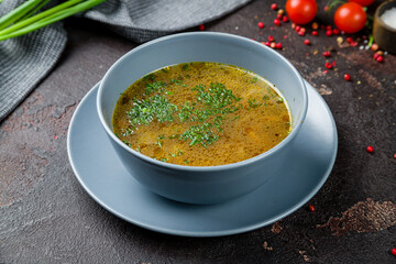 Chicken soup bouillon on blue bowl on dark concrete table