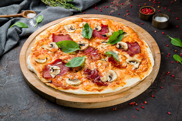 Pizza with ham and mushrooms on the board on dark concrete table