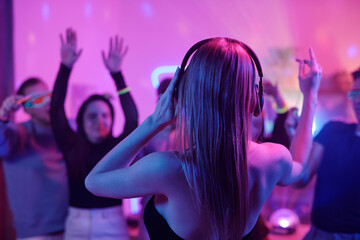 Back view of young woman with long blond hair touching headphones