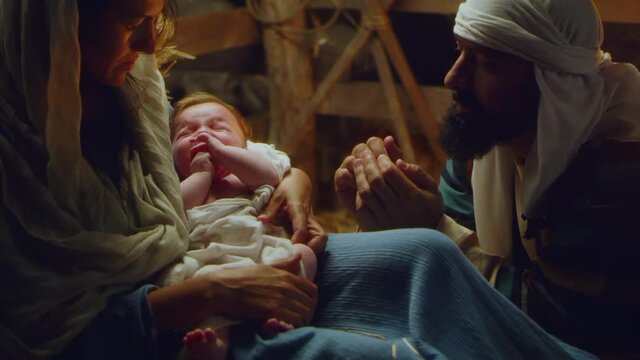 Joseph and Mary with crying baby Jesus near stalls nativity scene