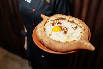 Top view on traditional Adjarian Khachapuri - open baked pie with melted salt cheese suluguni and egg yolk on wooden tray. Traditional georgian food