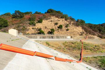 Orange floating debris boom, barrier on wall and ground of concrete dam of reservoir during dry...