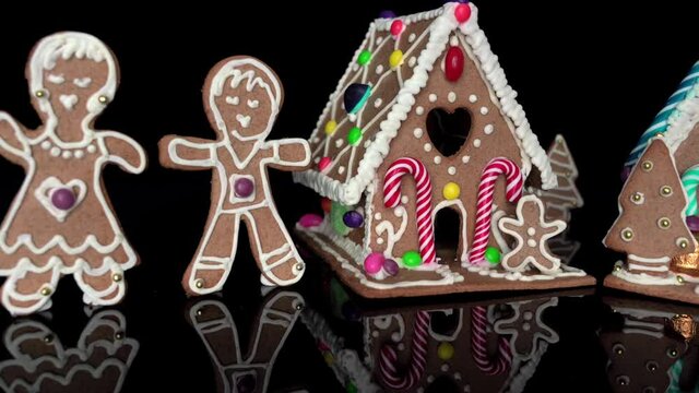Creative and original concept of beautiful Christmas gingerbread village on black background. Camera slides past decorated houses and people with xmas decorations. Fun, happy holiday season.