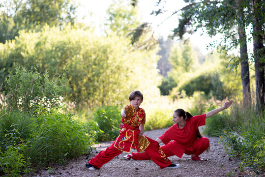 teenager girl with little boy in red sports wushu uniform are training in the park,  kung fu fighter children athletes, practicing wushu  in a forest