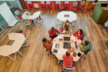 Medium group of young intercultural creative designers gathered by table
