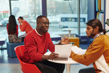 Two young contemporary intercultural businessmen in casualwear looking at paper