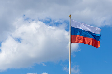 Russian tricolor waving in the wind, frontal view. The flag of the Russian Federation flutters against a blue sky with clouds. National symbol of Russia. Copy space