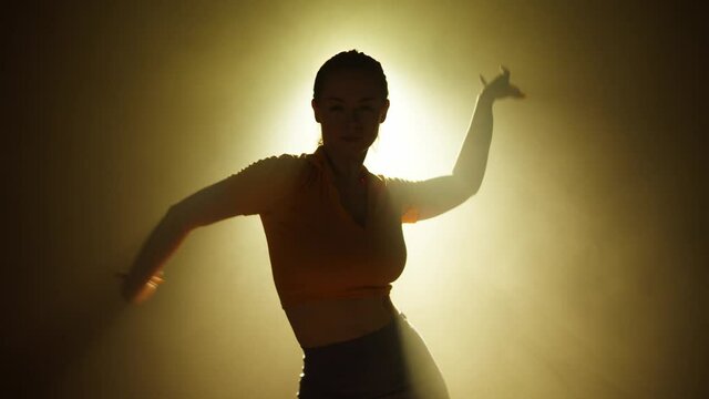 Young woman dancing on background with yellow light in studio. Shooting of modern slow dance with hands, choreography. Motion of female professional dancer expressing feelings in dance movings. 