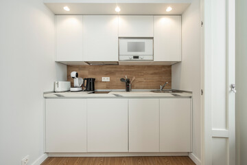 Fototapeta na wymiar Front view of small kitchen in white and oak wood tones, microwave and accessories included in a holiday rental apartment