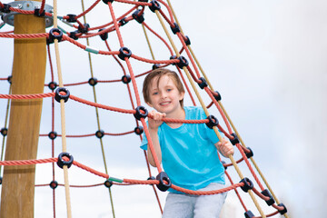 happy smiling boy climbs In Tie  Park, plays on a rope ladder, on a playground in the yard, park, outside