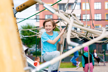 Fototapeta premium happy smiling boy climbs In Tie Park, plays on a rope ladder, on a playground in the yard, park, outside