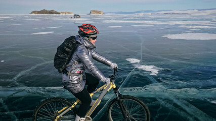 Woman is riding bicycle on the ice. Girl is dressed in a silvery down jacket, cycling backpack and...