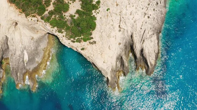 Top down drone shot of rocky coastline with cave and turquoise sea water.