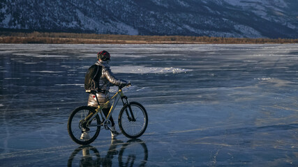Woman stands near her bike on ice. The girl cyclist stopped to rest. The beautiful view of the...