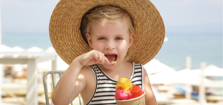 Adorable little girl eating gelato scoops in the beah bar. Summer vaction concept.